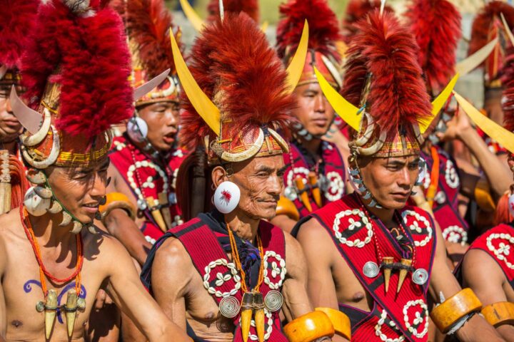 A group of men dressed in traditional attire with red feathered headdresses and yellow horn decorations participate in a cultural event, captivating travelers on an unforgettable tour filled with adventure.