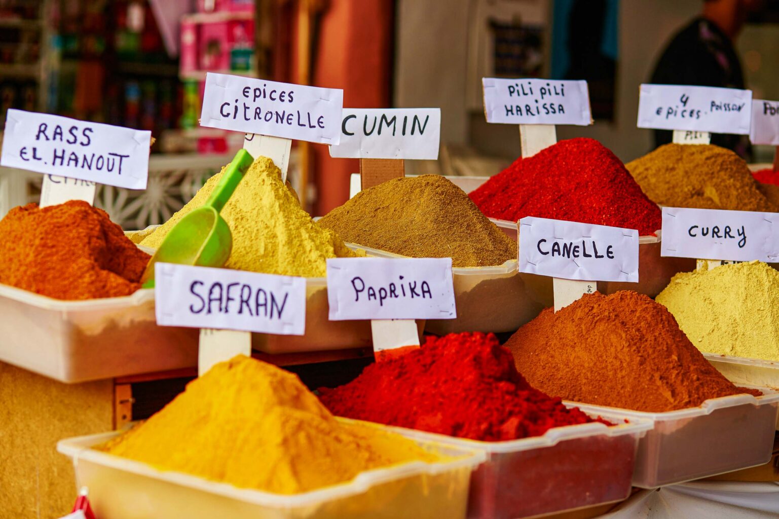 Small pyramids of red, yellow, and orange spices are labeled as curry, harissa, paprika, and other Moroccan specialties.