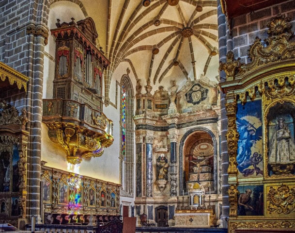 Interior of a richly decorated Portuguese church with ornate altars, colorful stained glass, intricate woodwork, and detailed stone architecture.