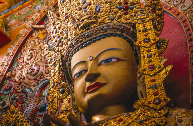 A close-up of an ornate golden statue adorned with colorful gemstones, depicting a deity with intricate details and a serene expression, set against a vibrant decorative background inspired by Nepalese artistry.