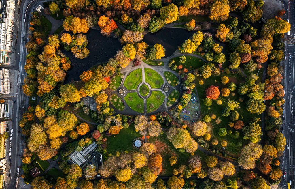 Aerial view of a Dublin park with symmetrical pathways, surrounded by autumn trees in various colors, a pond on one side, and a nearby road. Perfect for your list of things to do when exploring travel tips for the city.