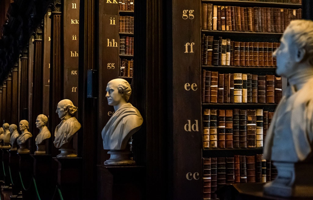 The library's interior, reminiscent of Dublin's rich history, features busts of historical figures on pedestals lining a wooden aisle. Shelves filled with old, leather-bound books and labeled sections in the background make it one of the city's must-see attractions.
