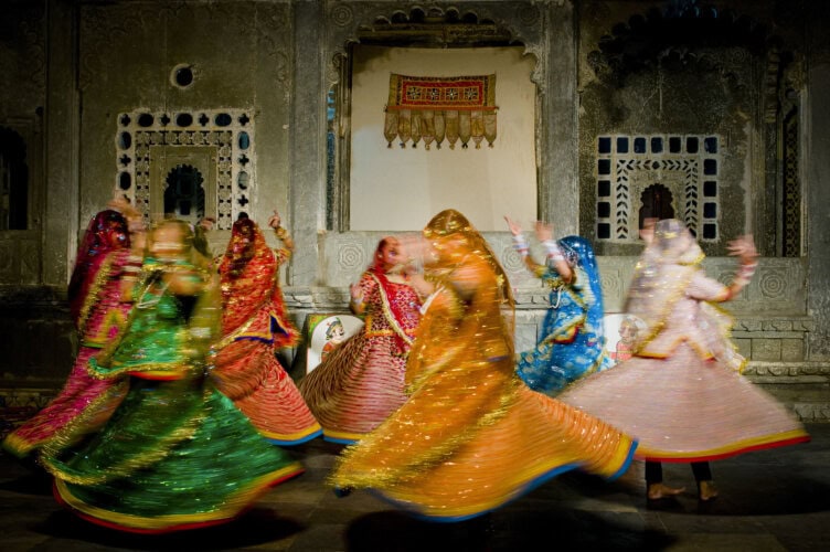 Dancers in colorful traditional attire perform a mesmerizing whirling dance inside a beautifully decorated stone building, capturing the vibrant spirit of Rajasthan.