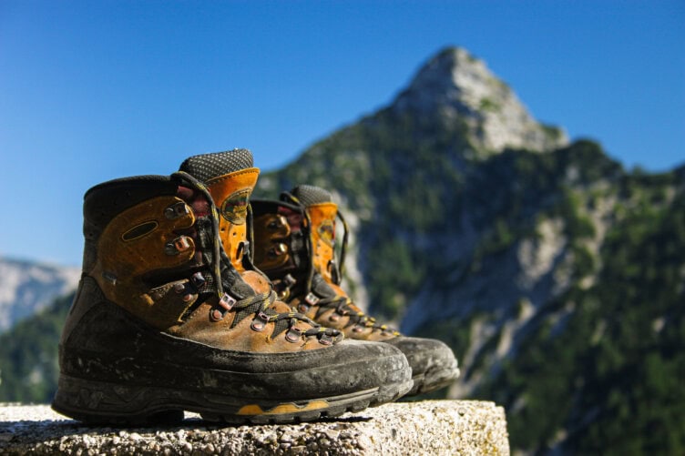 A pair of well-chosen hiking boots rests on a stone ledge, their wear telling tales of adventure. In the background, a mountain peak rises majestically against the clear blue sky, reminding every hiker of nature's call and the expert tips needed for each journey.