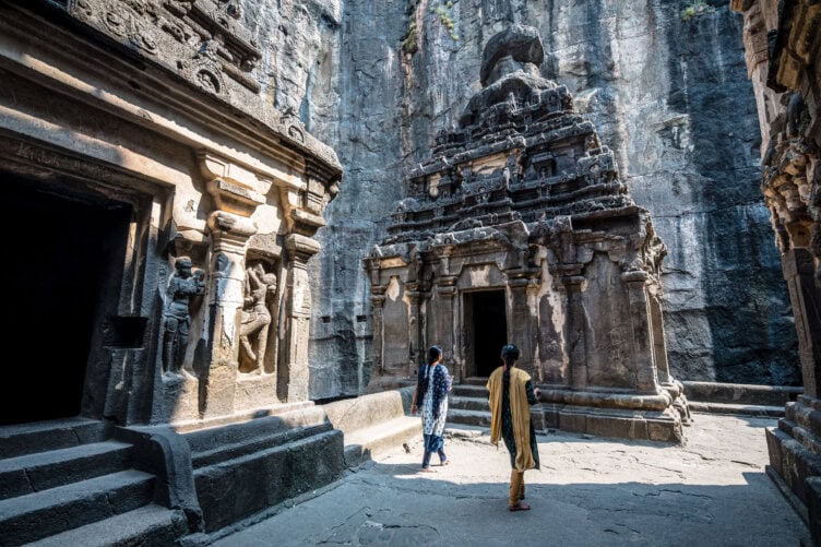 Two people explore an ancient stone temple in India, marveling at its intricate carvings and towering rock walls—a must-see on any travel itinerary.