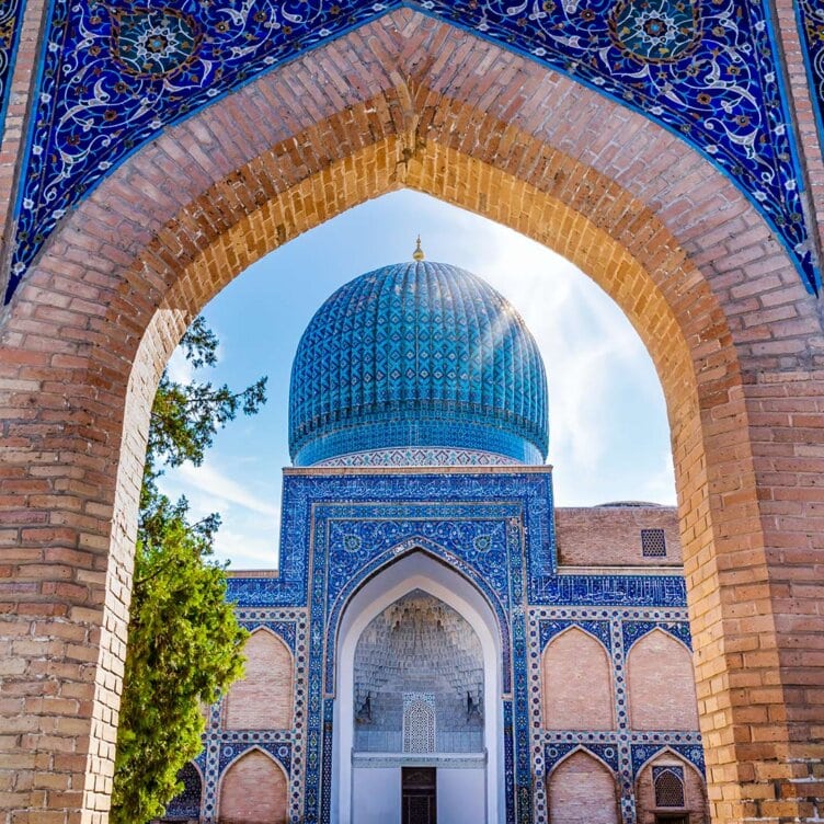 Archway view of an ornate blue-tiled dome and building, adorned with intricate geometric and floral patterns, set against a clear blue sky—a must-see spot for solo travelers looking to explore unique destinations on their top 8 trips list.