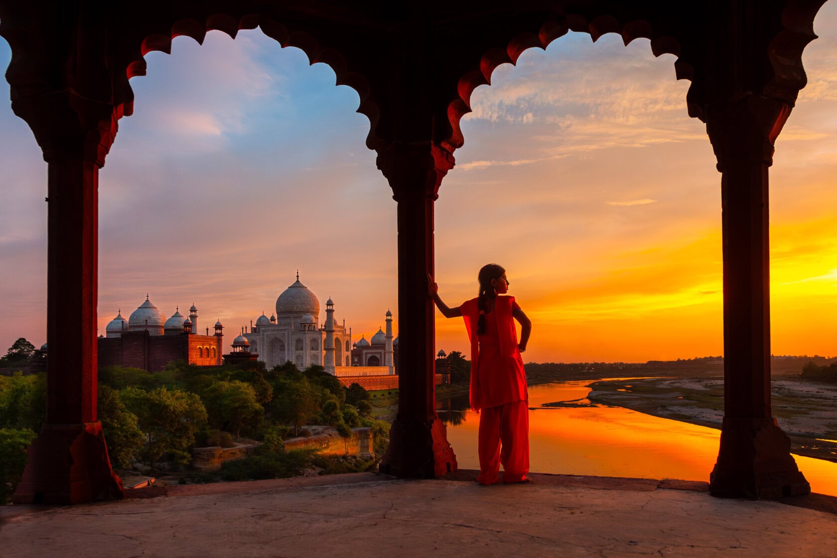 One of the top things to do in India is to witness the silhouette of a person standing under an arch, admiring the majestic Taj Mahal at sunset, its beauty mirrored perfectly in the river below.