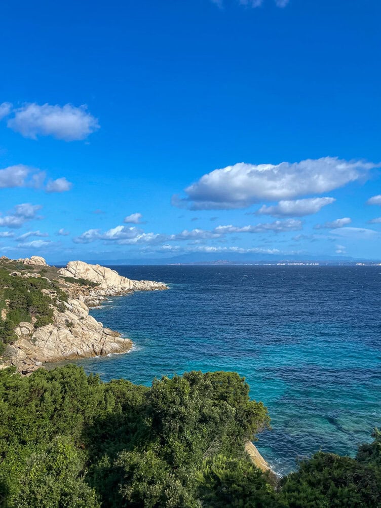 Experience the stunning coastal landscape of Corsica with its clear blue sky, rocky shoreline, and vibrant turquoise sea, all bordered by lush green vegetation. Perfect for hiking enthusiasts exploring the scenic trails of Corsica's captivating beauty.