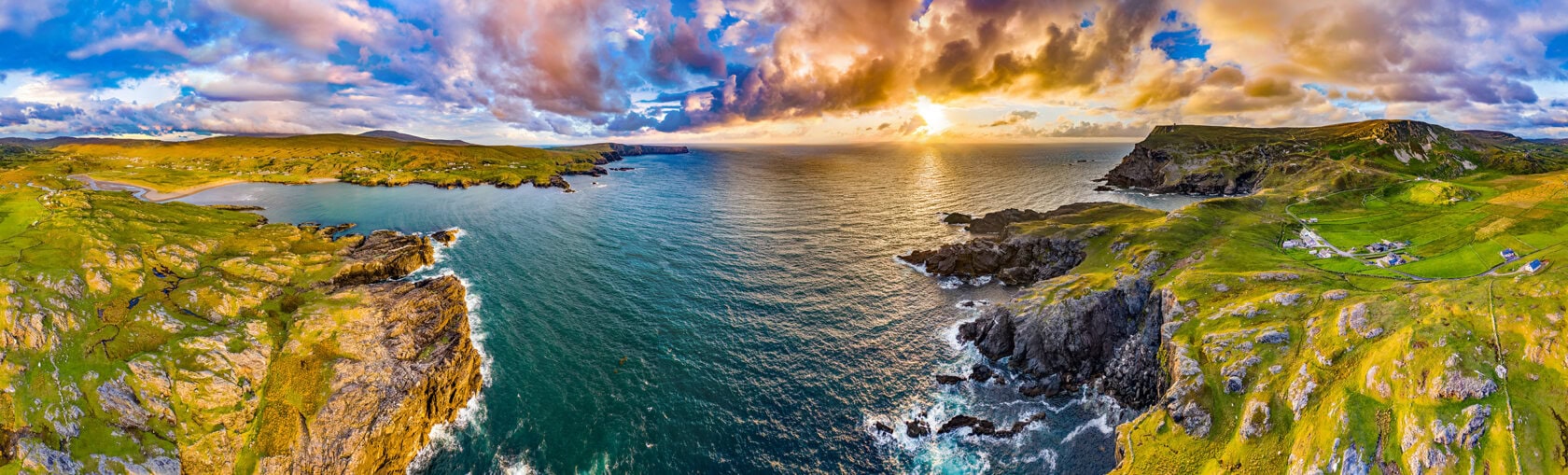 A panoramic aerial view of a rugged coastline with cliffs, green fields, and the ocean under a dramatic sky at sunset—perfect for an unforgettable hike or scenic tour.