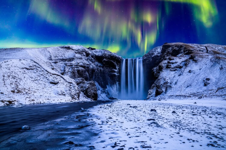 A snowy waterfall landscape with the northern lights glowing in the night sky above, perfect for an unforgettable winter hike.