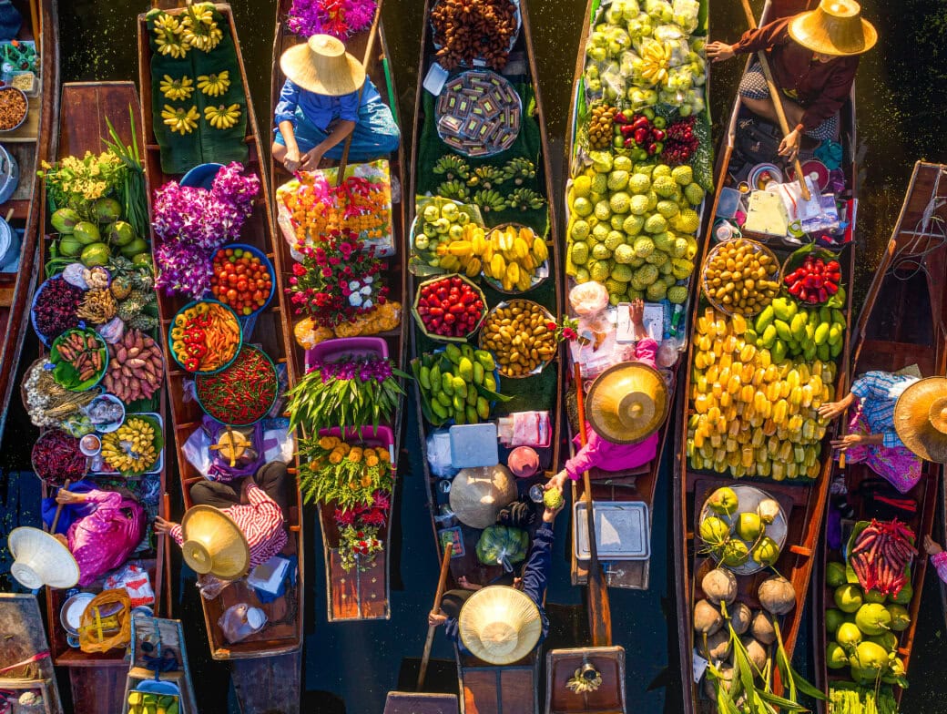Aerial view of a floating market, one of the top Bangkok attractions, with vendors in boats selling fruits, vegetables, flowers, and goods on the water.