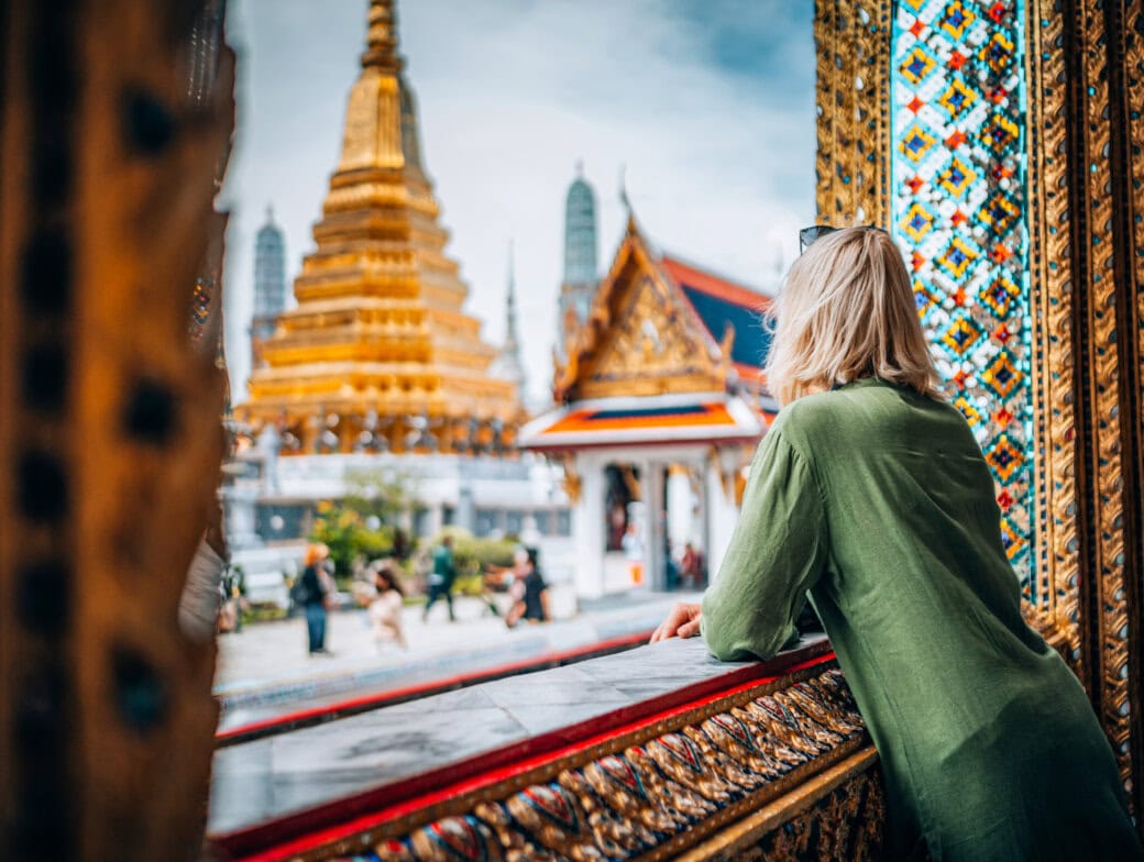 A person in a green shirt looks out at golden temple structures and ornate architecture, discovering Bangkok attractions at a cultural site—one of the top things to do in Thailand.